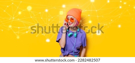 Young style girl in purple clothes with headphones and mobile phone on yellow background.  Clothes in 1980s style