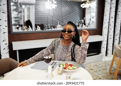 Young stylish african american woman, wear black sunglasses, sitting in restaurant, enjoying healthy food with wine. - Powered by Shutterstock