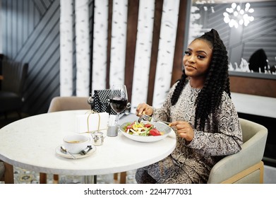 Young stylish african american woman sitting in restaurant, enjoying healthy food with wine. - Powered by Shutterstock