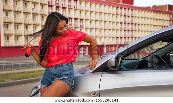 Young stylish african american woman posing by\
the car with keys. The concept of personal vehicles. Road safety.\
Driving courses