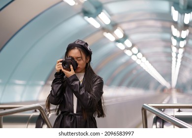 Young stylish asian girl make photos on camera in urban city transport riding escalator. Modern japanese female photographing while travelling. Creative chinese artist making pictures at underground