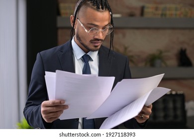 A Young Stylish Black Unusual Office Employee Examines The Received Documents, Carefully Examines Them. Young Boss With An Unusual Appearance In The Office