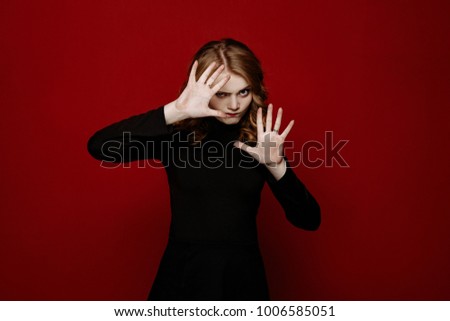young stylish blond  girl in black clothes posing in the studio isolated on red background, model tests, the girl emotionally poses