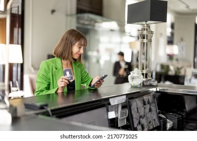 Young Stylish Business Woman Stands With Phone On Reception Of Luxury Hotel. Woman Check In Hotel During A Business Trip