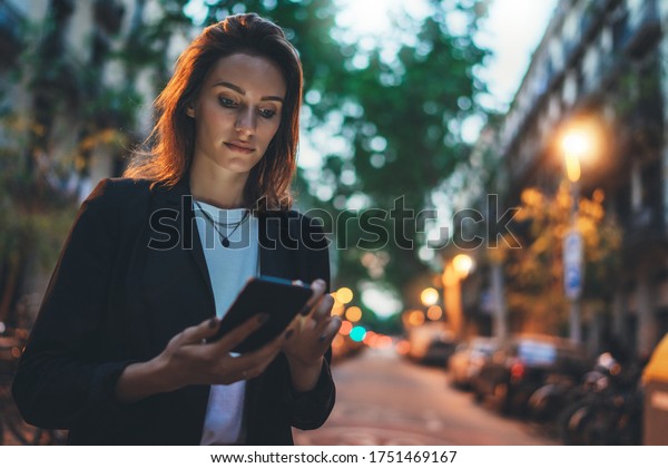 Young stylish business\
woman writes message on smartphone walking evening city street,\
hipster tourist traveling in european town and planning trip using\
mobile phone 