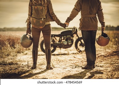 Young, stylish cafe racer couple on the vintage custom motorcycles in a field.
