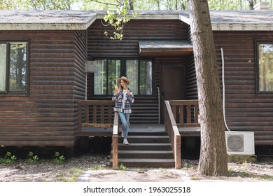 Young Stylish Caucasian Woman 30-35 Years Old Wearing Casual Clothing Shirt And Cowboy Hat. Influencer Using Social Media Via Mobile Phone. Person Enjoys Life At Morning During Summer Adventure In