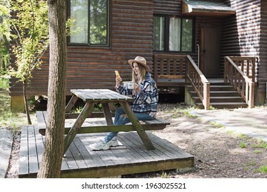 Young Stylish Caucasian Woman 30-35 Years Old Wearing Casual Clothing Shirt And Cowboy Hat. Influencer Using Social Media Via Mobile Phone. Person Enjoys Life At Morning During Summer Adventure In