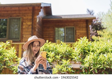 Young Stylish Caucasian Woman 30-35 Years Old Wearing Casual Clothing Shirt And Cowboy Hat. Influencer Using Social Media Via Mobile Phone. Person Enjoys Life At Morning During Summer Adventure In