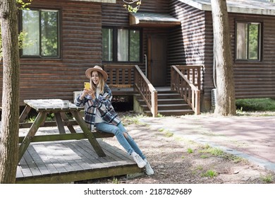 Young Stylish Caucasian Woman 30-35 Years Old Wearing Casual Clothing Shirt And Cowboy Hat. Influencer Using Social Media Via Mobile Phone. Person Enjoys Life At Morning During Summer Adventure In