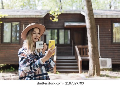 Young Stylish Caucasian Woman 30-35 Years Old Wearing Casual Clothing Shirt And Cowboy Hat. Influencer Using Social Media Via Mobile Phone. Person Enjoys Life At Morning During Summer Adventure In