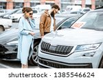 Young stylish couple choosing luxury car to buy on the open ground of the dealership