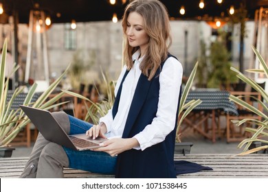 Young Stylish Fashion Blogger Using Laptop For Work While Sitting Outside On A Bench, Beautiful Busy Woman Typing On Portable Computer For Distance Job, Businesswoman Working On Pc In The Fresh Air 