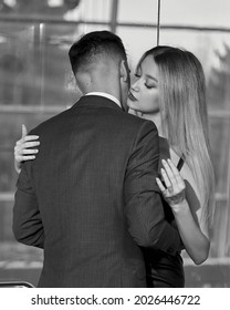 Young Stylish Fashionable Caucasian Couple Hugging And Kissing In Hotels Elevator. Handsome Man In Classical Suit And Blonde Pretty Woman In Black Dress