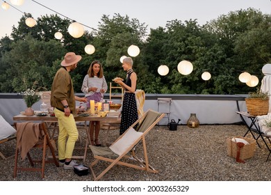 Young stylish friends hang out together talk and having fun on a the beautifully decorated rooftop terrace at dusk. People at open air party