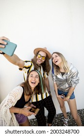 Young Stylish Friends Have Fun, Taking Selfie Photo On Phone On A White Background. Millennials Or Gen Z Spend Time Together With Digital Gadgets