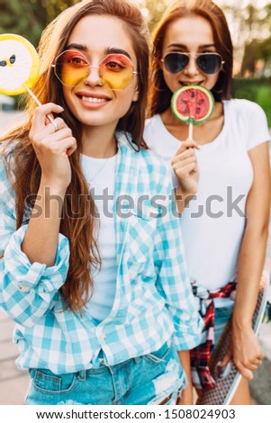 Young stylish funny girls with lollipops, grimace and have fun in the city in Sunny weather