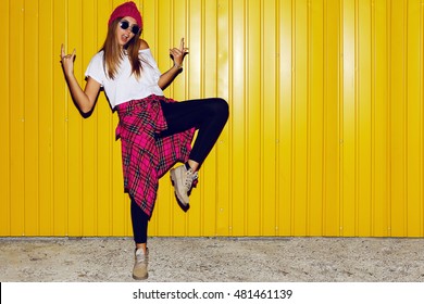 Young stylish hipster  girl having fun   and doing grimaces  near bright yellow urban wall at night with flash. Wearing pink hat, warm hipster boots.  - Powered by Shutterstock