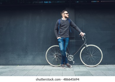 A young stylish hipster posing next to his bicycle.