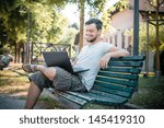 young stylish man using notebook at the park