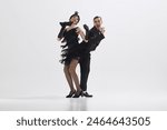 Young stylish man and woman dressed in 1920s attire perform lively Charleston dance isolated over white studio background. Concept of art, retro and vintage, hobby, entertainment, 20s