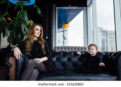 Young Stylish  Mother With Her Adorable Baby Girl In  Hipster Cafe. A Fashion Mom And Toddler. Sitting On A Leather Couch. Overbearing Mother And Hamming Daughter