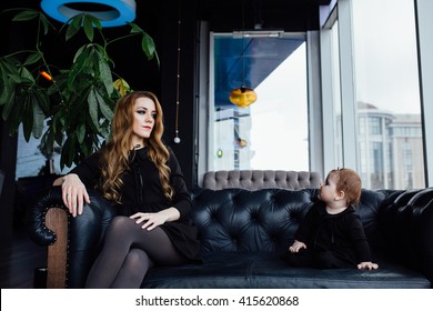 Young Stylish  Mother With Her Adorable Baby Girl In  Hipster Cafe. A Fashion Mom And Toddler. Sitting On A Leather Couch. They Are Looking At Each Other, Awkward Pause, Stress