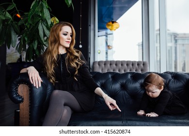 Young Stylish  Mother With Her Adorable Baby Girl In  Hipster Cafe. A Fashion Mom And Toddler. Sitting On A Leather Couch. Overbearing Mother