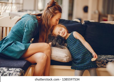 young and stylish mother with long hair and a green dress playing with her little cute daughter and little black rabbit at home