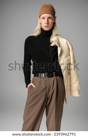 young stylish non binary model posing with winter jacket and one hand in pocket, fashion concept