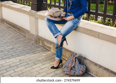 young stylish pretty woman, hands holding a phone, denim shirt and jeans, high heel shoes, hat, backpack, sunny day, good weather, city street, vacation europe, travel, detail, cool accessories