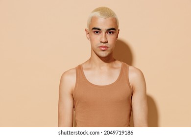 Young Stylish Serious Blond Latin American Hispanic Gay Man 20s With Make Up In Beige Tank Shirt Looking Camera Isolated On Plain Light Ocher Background Studio Portrait People Lgbt Lifestyle Concept