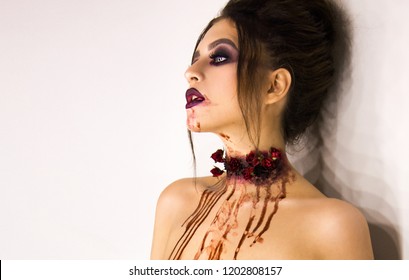 young stylish sexy brunette girl with halloween bloody makeup is standing and looking straight on white wall background in the studio, portrait