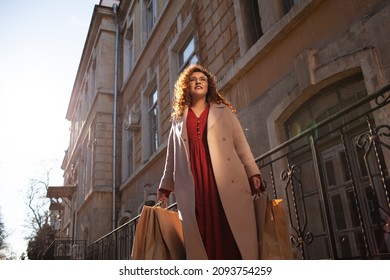 Young stylish woman with curvy hairs, wearing stylish trendy outfit, red dress and coat, walking in the street in cold season. Overweight model
