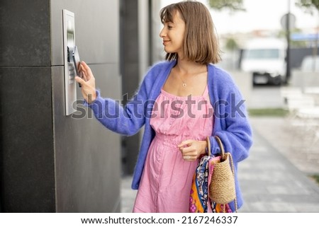 Young stylish woman getting access to the building by attaching smartphone to intercom. Concept of modern security technologies for access and smart home
