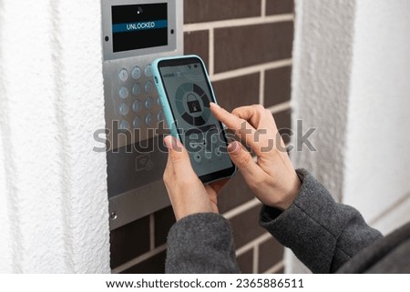 Young stylish woman getting access to the building by attaching smartphone to intercom. Concept of modern security technologies for access and smart home