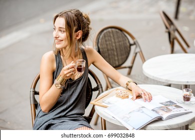 Young stylish woman in gray dress drinking coffee outdoors at the cafe in Paris