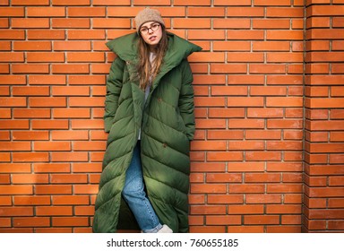 Young Stylish Woman In A Green Down Jacket On City Street By The