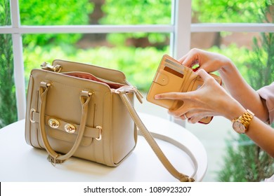Young stylish woman hand holding brown wallet with credit card take out money for pay in restaurant. Beige color leather handbag put on white table background.