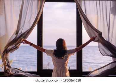 Young stylish woman opens the curtains. Towards a new life and a dream concept. Early morning meeting dawn is a great mood. Sunrise on vacation trip. Seascape ocean outside. Window of Opportunities - Powered by Shutterstock