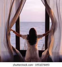 Young stylish woman opens the curtains. Towards a new life and a dream concept. Early morning meeting dawn is a great mood. Sunrise on vacation. Seascape outside the window. Window of Opportunities