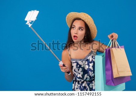 Young stylish woman posing and taking a selfie on the phone with shopping bags on a blue background