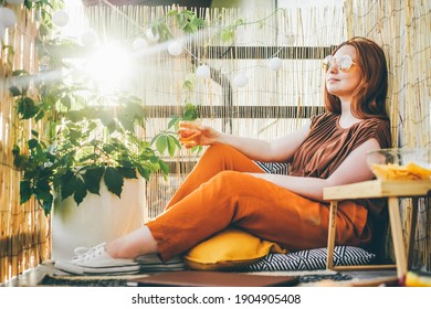 Young stylish woman sitting and holding cocktail on modern terrace.