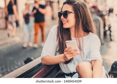 Young Stylish Woman Using Phone Sitting On The Street.