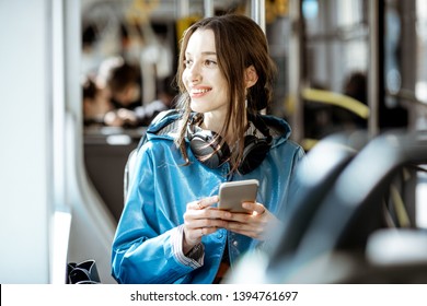 Young Stylish Woman Using Public Transport, Sitting With Phone And Headphones In The Modern Tram
