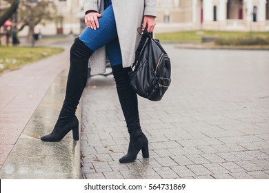 young stylish woman walking in autumn city, cold season, wearing high heeled black boots, leather backpack, accessories, grey coat, fashion trend, legs close-up details