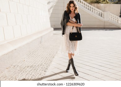 Young Stylish Woman Walking In Street In Fashionable Outfit, Holding Purse, Wearing Black Leather Jacket And White Lace Dress, Spring Autumn Style, Posing, High Leather Boots