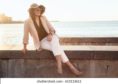 Young Stylish Woman Wearing Neutral Blazer And Hat Walking On The City Street At The Afternoon. Casual Fashion, Elegant Look. Plus Size Model.