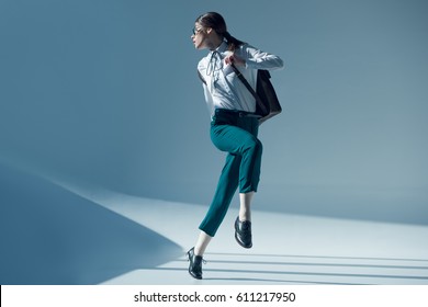 young stylish woman in white shirt, green trousers and glasses looking away while jumping