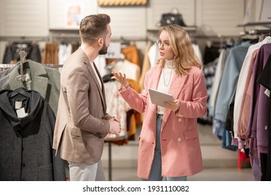 Young stylist using digital tablet while talking to the customer in the clothing shop in the mall - Powered by Shutterstock